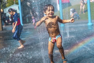 Happy child running through jets of water in a playful splash park on a hot summer day in