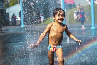 Happy muddy child playing and running through jets of water in a playground water park fountain in