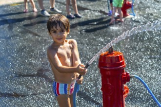 Happy child playing with water jet from a red fire hydrant during a hot summer day in vancouver,