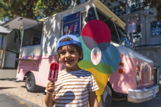 Little boy enjoying a colorful popsicle on a sunny day, standing near a vibrant ice cream truck in