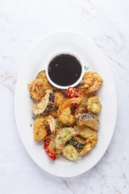 Shrimp and assorted vegetables are deep fried in a light batter and served on a white plate. A