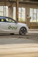 A white car with car sharing logo is parked in a hall with large windows, Deer E-Car Sharing,