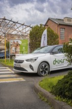 Opel with car sharing logo stands in front of an advertising banner in an urban setting with