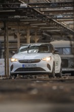 White Opel with car sharing logo in an urban industrial building with visible metal structures,