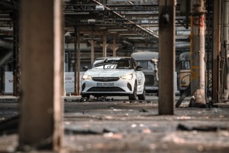 A car is parked in an empty, structured factory building, accentuated by light and shadow, Deer
