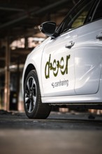 Side view of a white car sharing vehicle in an industrial environment, Deer E-Car Sharing,