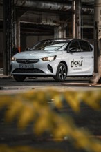 White Opel car sharing vehicle in industrial plant with yellow foreground, Deer E-Car Sharing,
