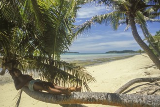 Boy lying on a coconut tree on the beach of Tavewa Island, Yasawa Islands, Fiji