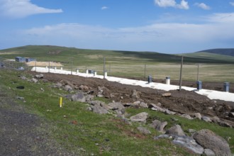 Wide landscape with green field and blue sky, in the foreground a road and a covered railway track,