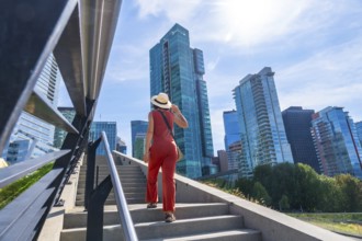 Young woman with hat and orange jumpsuit climbing stairs in vancouver downtown with modern