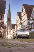 White Renault car in an old town with half-timbered houses and church tower in the background, Deer