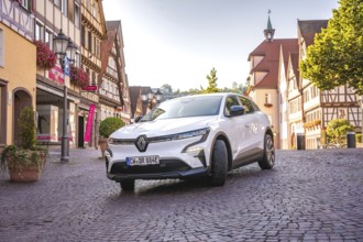 White car on a paved road in a European city center in sunshine, Deer E- car sharing, Renault