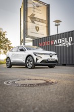 A white electric car is parked in front of a Motorworld sign on a sidewalk, Deer E- Carsharing,