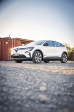 A white electric car stands in front of a container on a gravel field at dusk, Deer E-Carsharing,