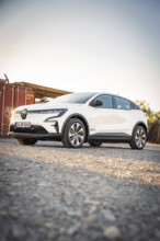 A white electric car is parked on a dirt road in the evening light in front of a container, Deer