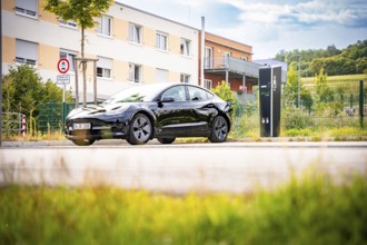 Black car at a charging station in a sunny, urban area, Deer e-Carsharing, Tesla Model 3, Calw,