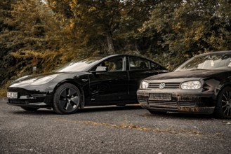 Two black cars side by side in a parking lot with an autumn tree backdrop, Deer e-Carsharing, Tesla