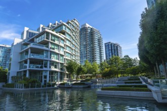 Modern glass and concrete buildings stand tall, reflecting in the calm water of a city park,