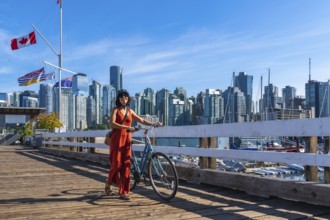 Female tourist walking with her bicycle on a wooden pier, enjoying vancouver downtown skyline in