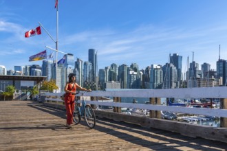 Tourist walking with her bicycle on a wooden pier with canadian and british columbian flags waving