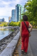 Female tourist wearing red jumpsuit walking along waterfront promenade in vancouver, british