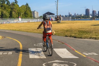 Tourist enjoying cycling in kitsilano beach park with english bay and the city of vancouver skyline