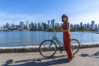 Young woman wearing a helmet stands next to her bicycle, enjoying a scenic waterfront view of