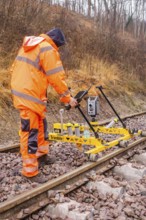 Construction worker with measuring device device works on yellow equipment on rails in winter,