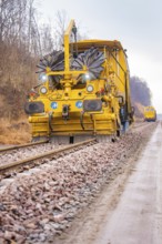 Yellow track construction machine on a railroad track in use on a construction site, tamping