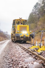 Yellow rail vehicle on tracks in foggy forest landscape, surrounded by tools, stuffing machine on