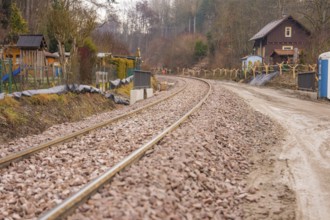Railway tracks through quiet rural area with houses and trees in the background, stuffing machine