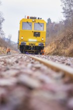 Yellow train on dirt road through forest with workers in the background, stuffing machine on