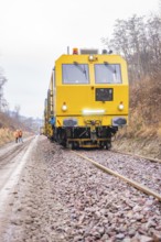 Yellow rail vehicle travels on gravel tracks through wintry landscape with workers, stuffing