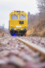 Yellow vehicle on gravel with construction workers in the forest, tamping machine on Hermann,