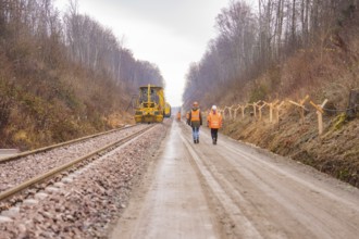 Construction worker and machine tool working on a railroad track in the forest, tamping machine on