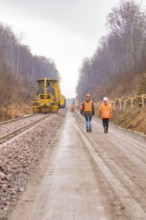 Construction worker on a rail line in the forest, accompanied by a yellow machine, tamping machine