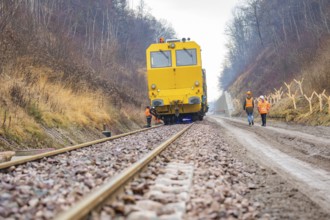 Yellow vehicle on rails with construction workers on a gravel path in the forest, stuffing machine