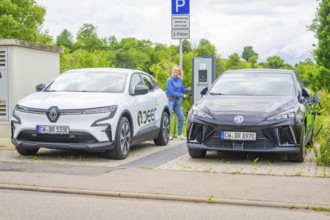 Two electric cars are parked at the outdoor charging station with a woman nearby, Deer E-