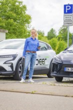 Woman standing in front of two electric cars in a parking lot with technological flair, Deer