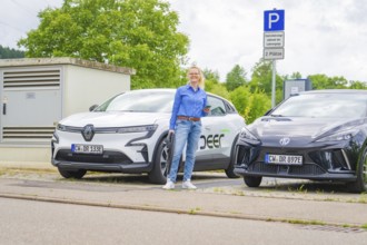 Two electric cars park side by side at a charging station, surrounded by green countryside, Deer