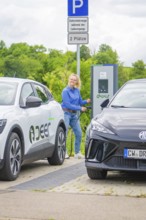 Woman refuels electric car at a charging station between two parked vehicles, Deer E-Carsharing,