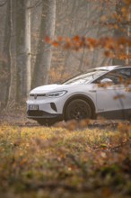 A white car drives on a forest path surrounded by autumn trees, Deer E-Carsharing, VW ID4, Calw,