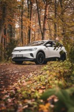 A white SUV on a forest path surrounded by autumn trees and foliage, Deer E-Carsharing, VW ID4,