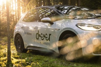 A car is parked in the forest, surrounded by sunlight and nature, promoting car sharing, deer e-car