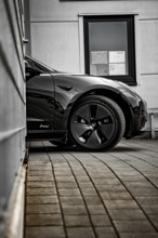 Black car in front of a modern building with tiled floor and a window, Deer E-Carsharing, Tesla