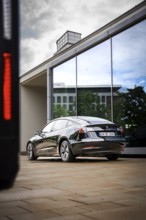 Black car in front of a modern glass façade reflecting the sky, Deer E-Carsharing, Tesla Model 3,