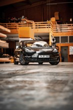 Black car in an industrial-looking workshop with wooden details, parked on concrete floor, deer