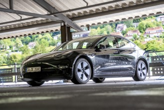 Black car in a bright, covered parking garage with views of green hills, Deer E-Carsharing, Tesla