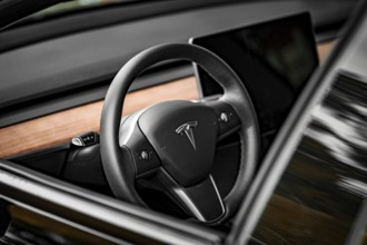 Close-up of a black steering wheel with wood paneling in modern car interior, Deer e-car sharing,