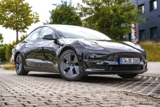 Black car on an urban road in front of modern buildings and trees, Deer E-Carsharing, Tesla Model